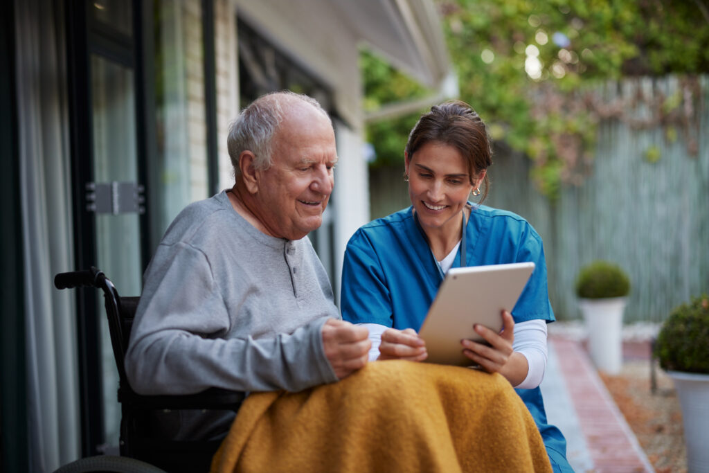 Senior man getting help with tablet from female caregiver